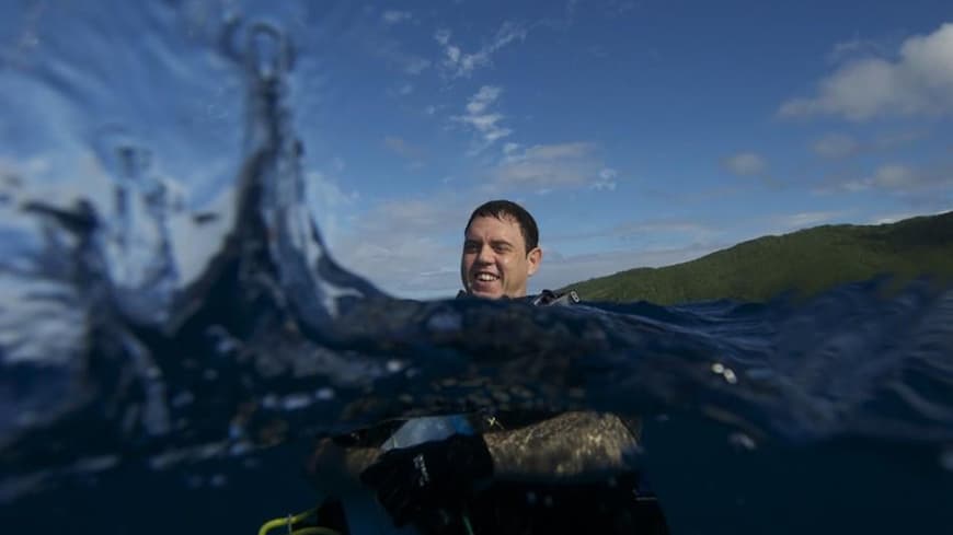 Aaron Jenkins diving in the ocean above coral reef