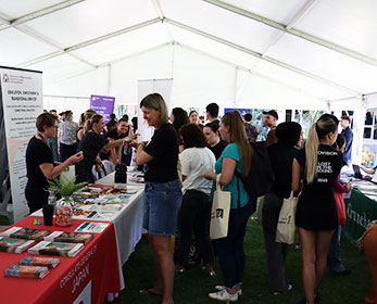Students interacting with partners at their stalls at the school of education careers fair holding tote bags and smiling