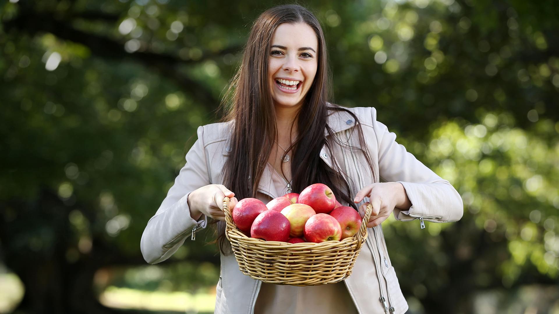Young woman facing camera and holding a basket of apples