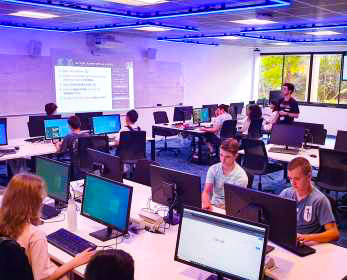 Male student using a computer mouse to assist another student on a computer