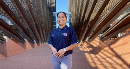 Student in navy blue short sleeve t-shirt standing in shade of a building