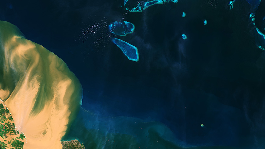 A satellite image showing muddy water flowing from a river into the blue waters of the Coral Sea and Great Barrier Reef.
