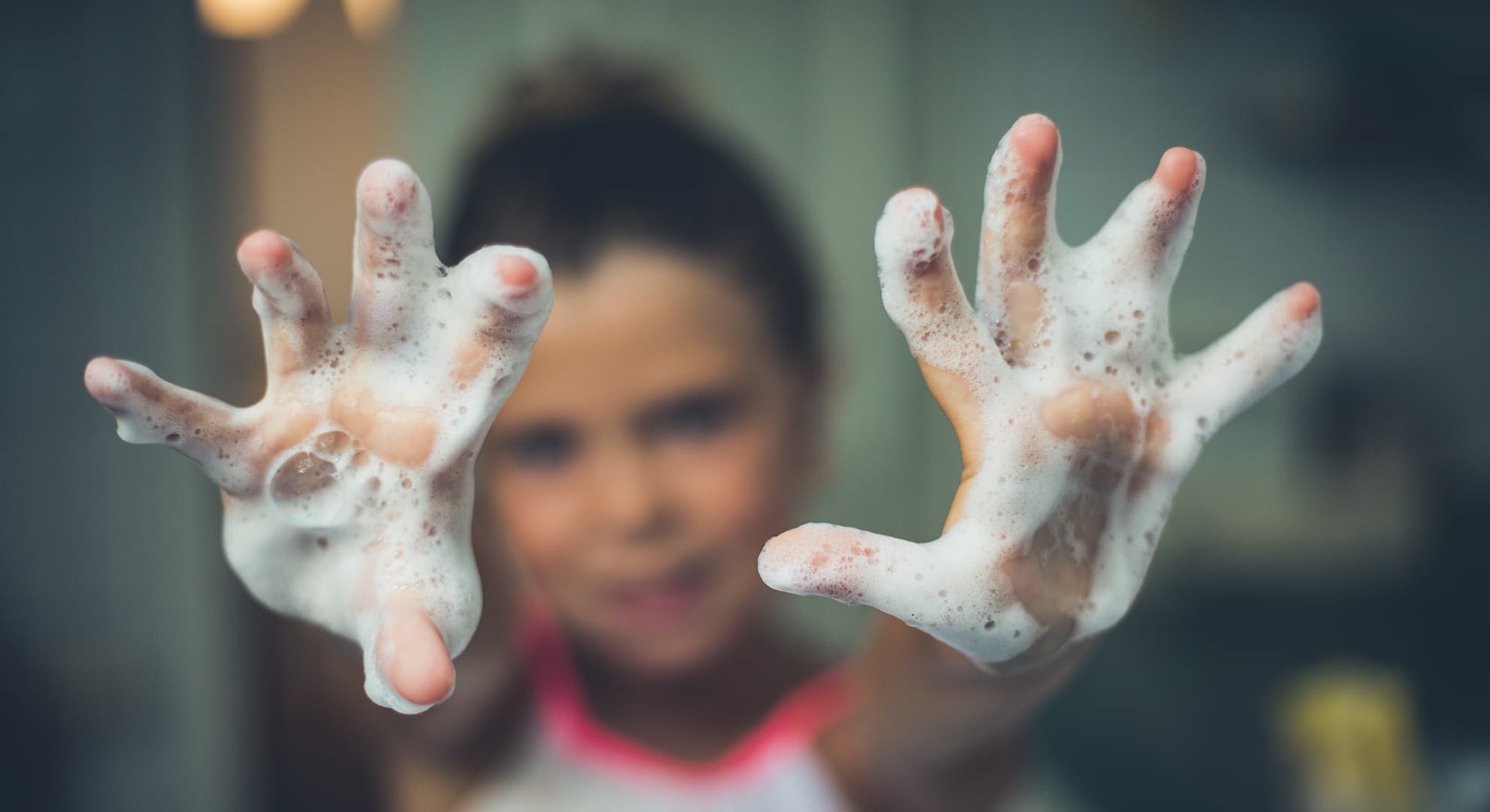 Young girl holding her soapy hands up to the camera.