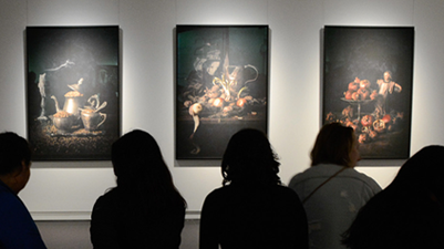 A group of people admiring three Queens and Conquests paintings.