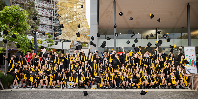 Childrens University graduates standing on the steps at ECU Joondalup celebrating and throwing their hats at the 2023 graduation
