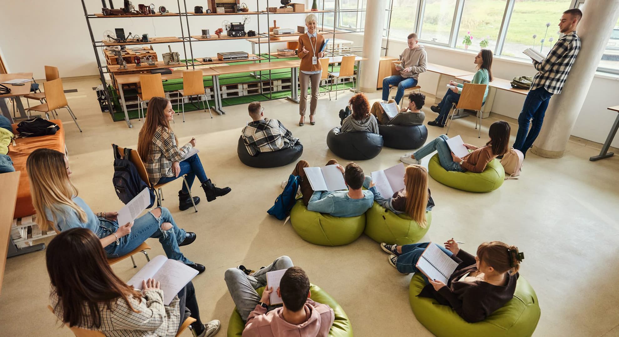 Female teacher standing in an open plan classroom with students spread out sitting on beanbags.