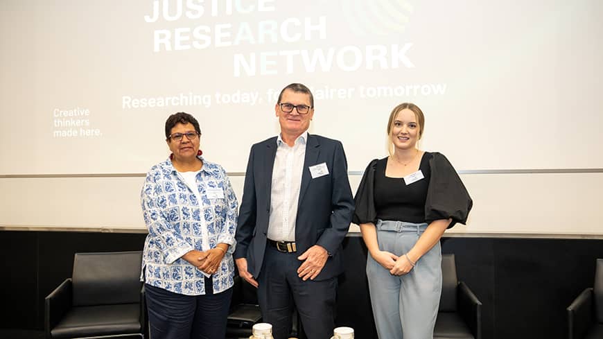 Group shot of three people facing the camera in front of a large screen