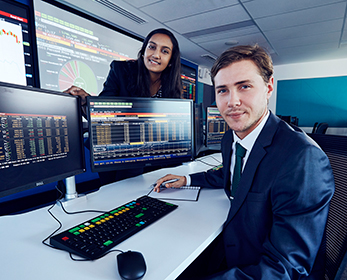 Two students in the SMART lab, computer monitors with financial data displayed.