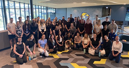 A group of 50 people standing in front of a large. yellow eagle icon