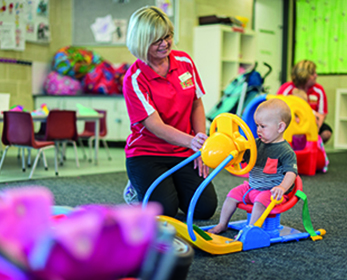 A woman plays a game with a small child in the creche