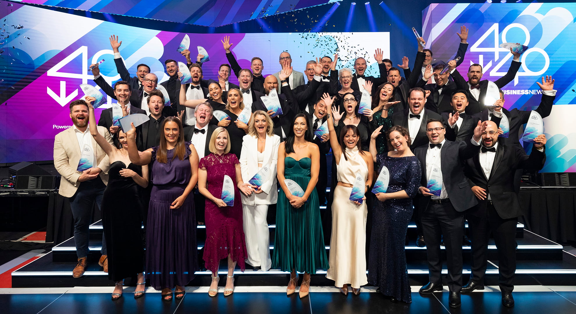 A group of business and community leaders throw their hands up in celebration on a stage.