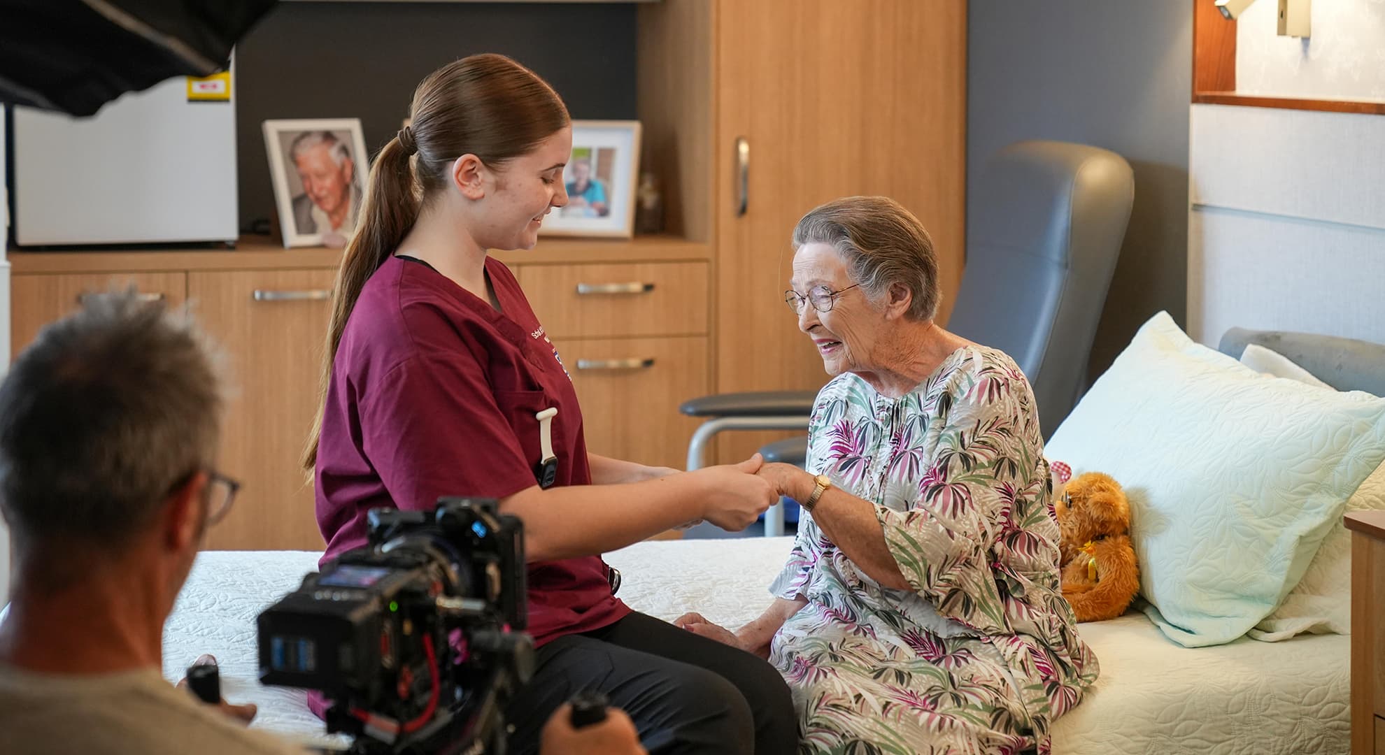 A young nursing student helps an aged care resident rub lotion on her hand. They are in the middle of being filmed for a corporate video story.