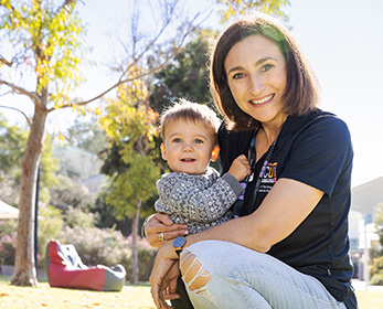 ECU Staff Giver Amy Blundell smiling outside holding her son Taj.