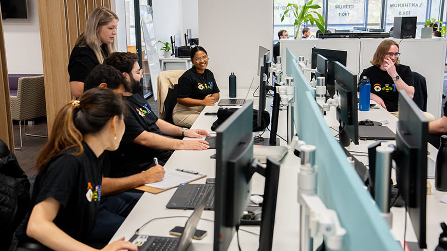 Interns sitting at computers in the lab smiling.