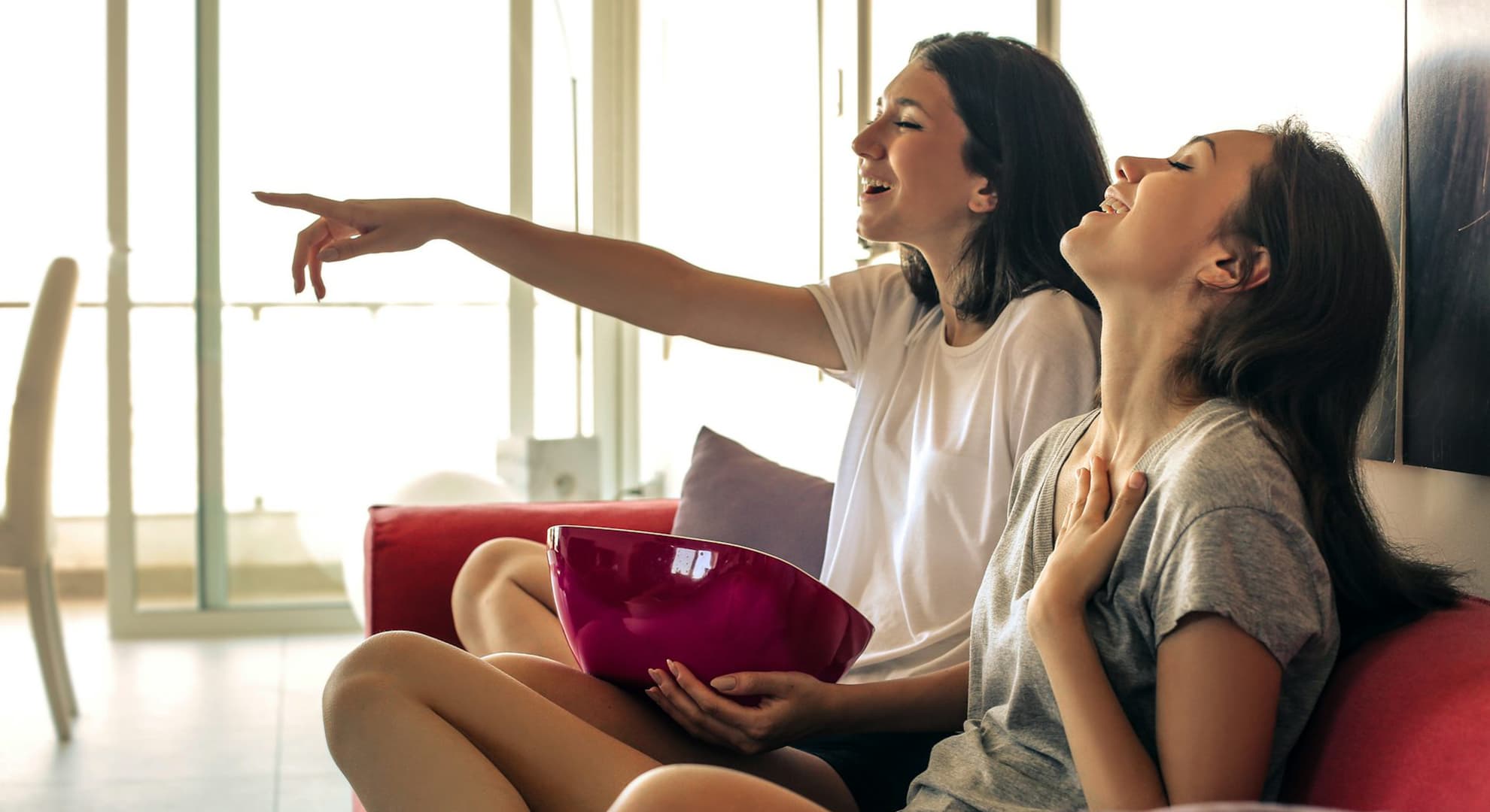 Two young people watching bloopers on the TV and laughing.