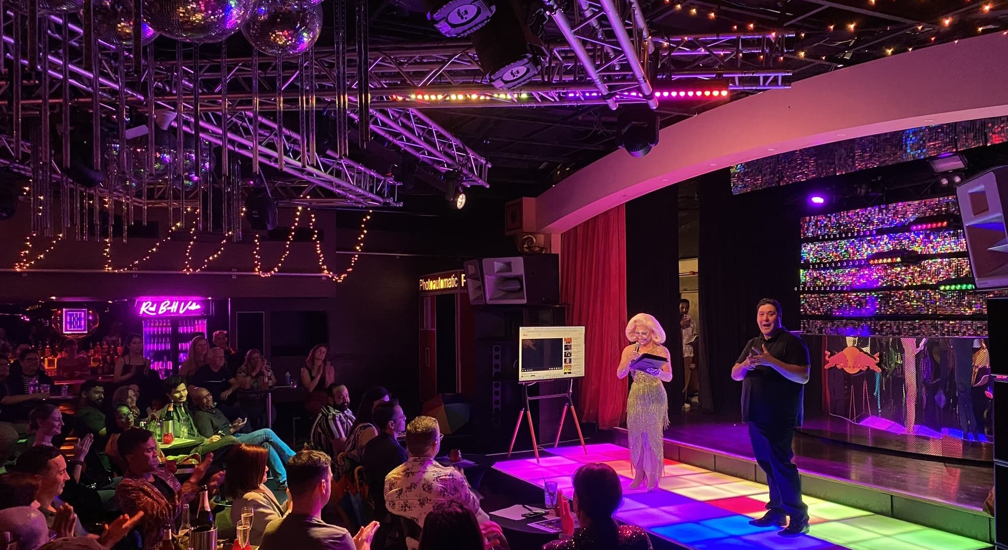 Theatre show with announcers on stage and audience seated at tables