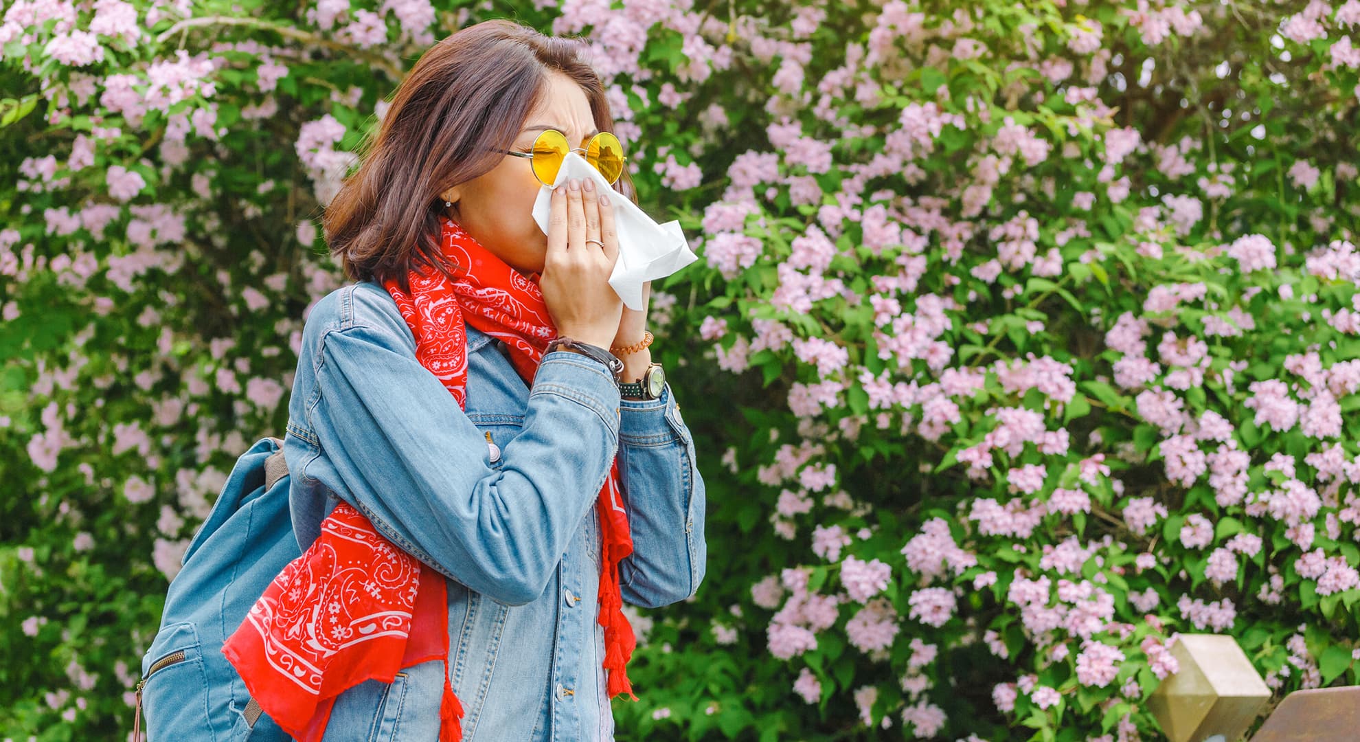 Lady in glasses blowing her nose near a blooming tree.