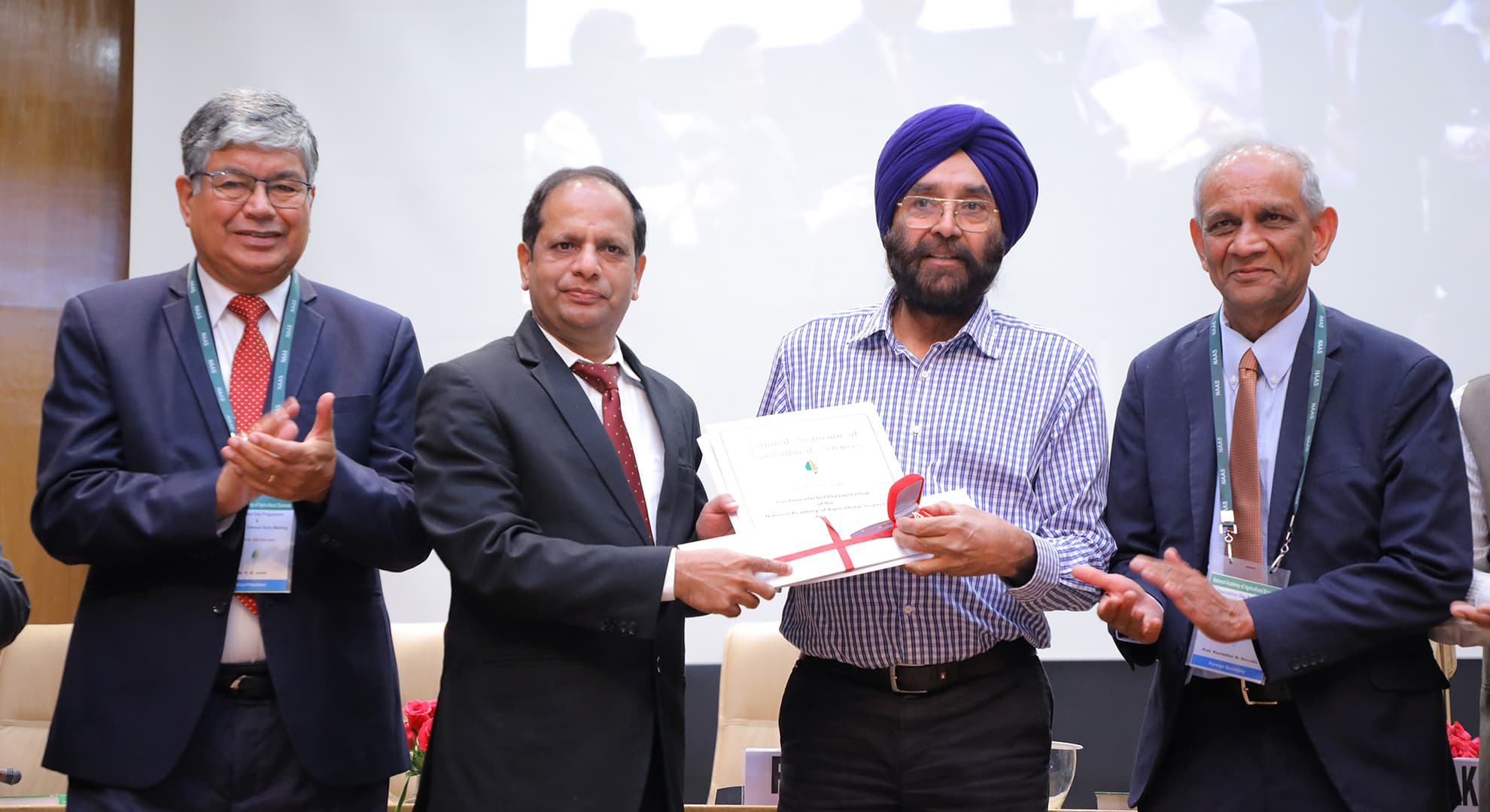 Group of four men in suits standing together with certificate being presented