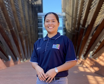 Student in navy blue short sleeve t-shirt standing in shade of a building