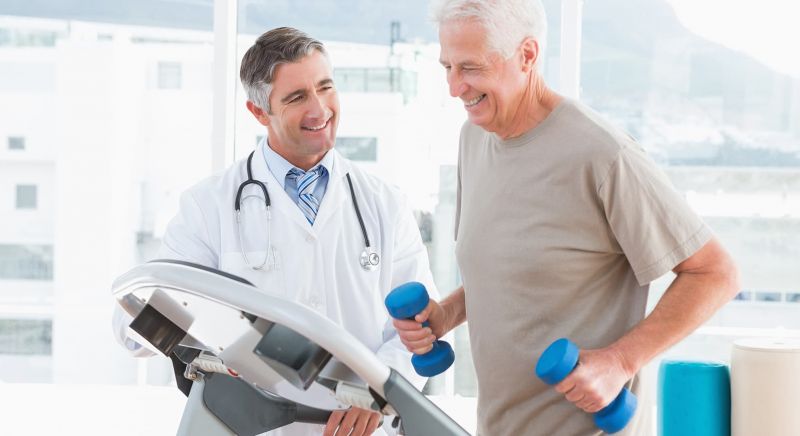 Senior man on treadmill with therapist in fitness studio