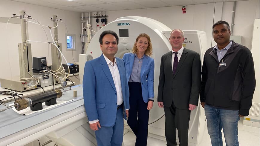 Researchers and embassy representatives stand in front of a CT scanner in a lab.