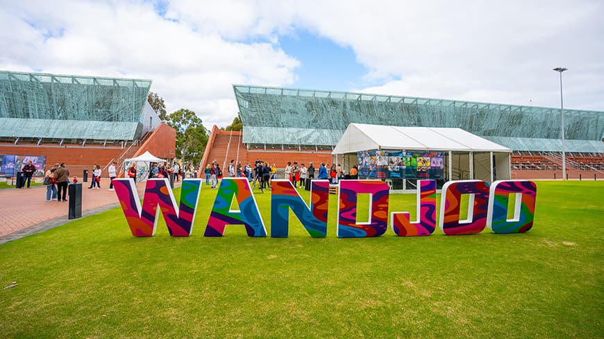 Colourfully patterned blocks of letters that spell out \'wandjoo\' sitting on green grass at ECU Joondalup.