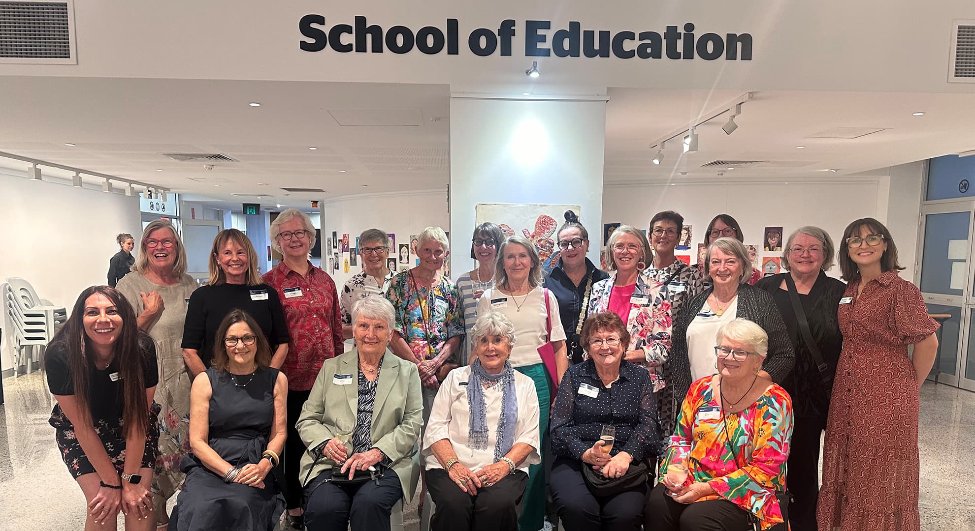 A group of ECU alumni sit together with staff and community members, above them there is a sign that says School of Education.