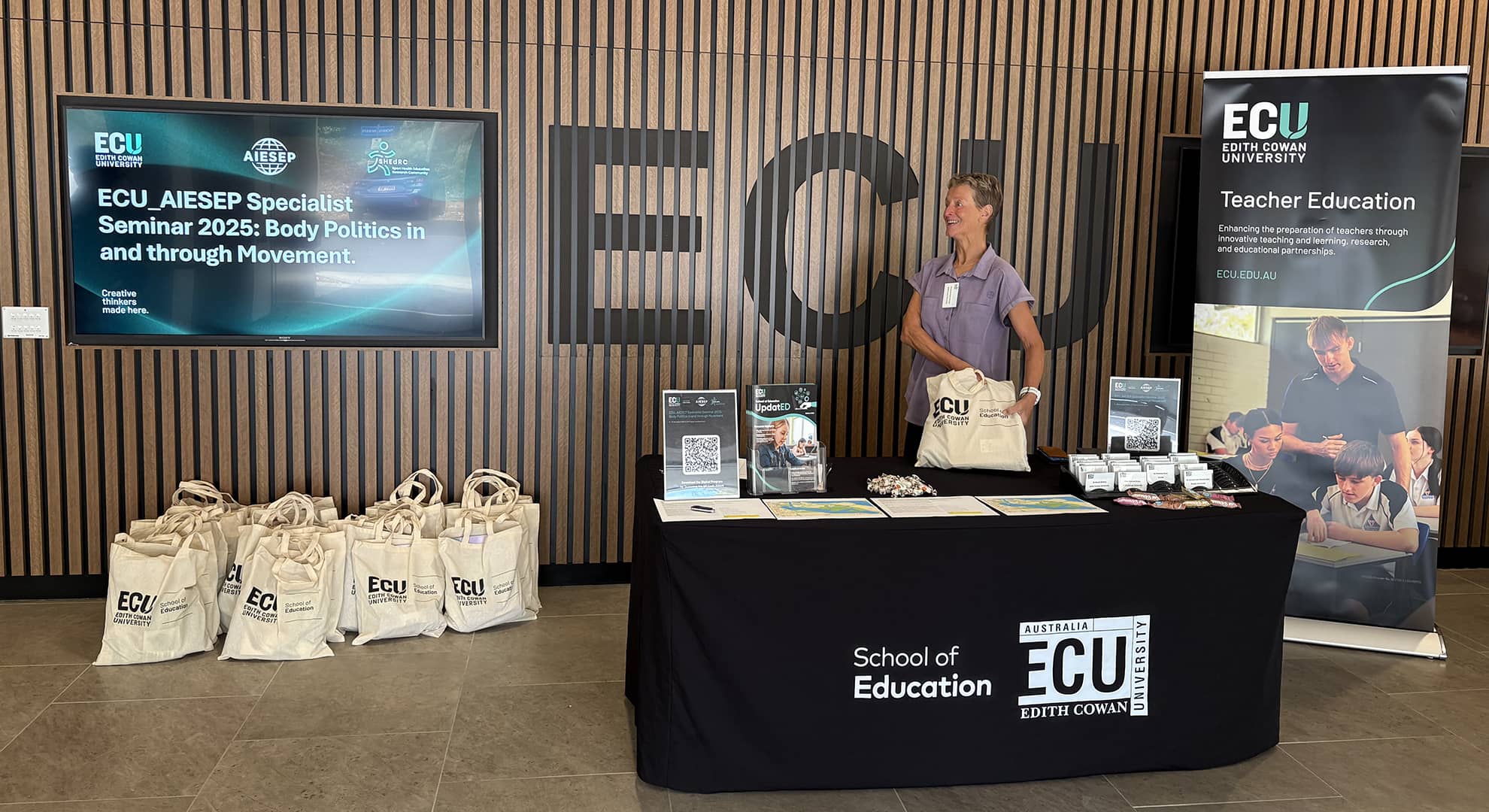 Woman standing behind low table with ECU Branding around her.