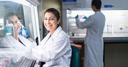 Woman in white lab coat in a science laboratory holding equipment.