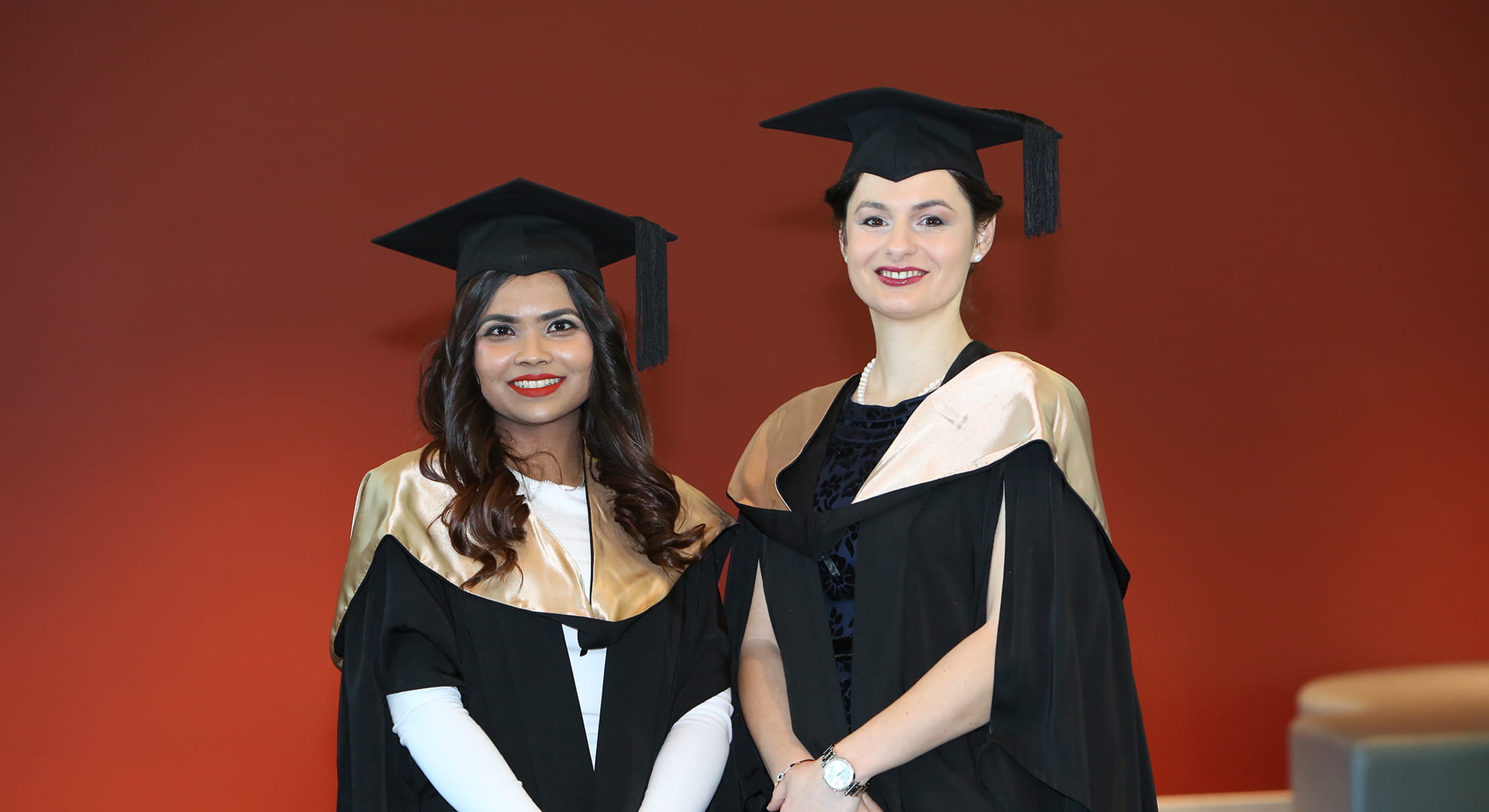 ECU students Maisha Zuhair and Andra Dinu standing together in their graduation regalia