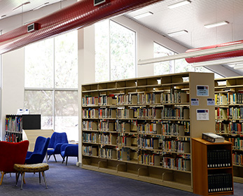 A wideshot of the ECU South West Campus Library, showing a space with high ceilings, lots of natural light, shelves full of books, and couches and tables dotted around, inviting peaceful reading and study.
