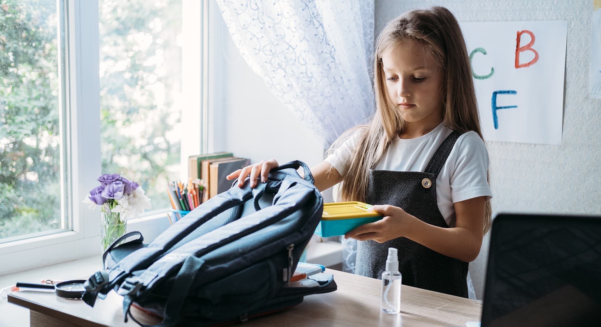 Young girl putting her lunch into a school bag.