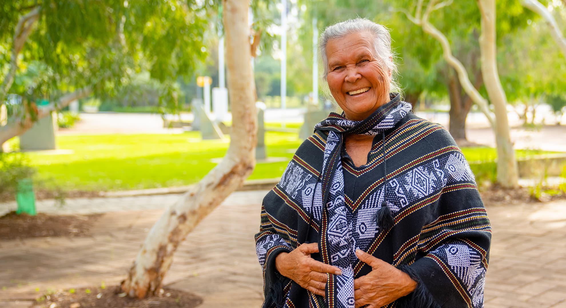 Roma Winmar wears a black and purple fringed poncho, she grins and looks happy outdoors.