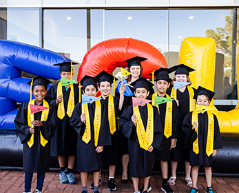 Children's University members celebrating in their graduate robes and mortar boards, holding coloured CU flags.