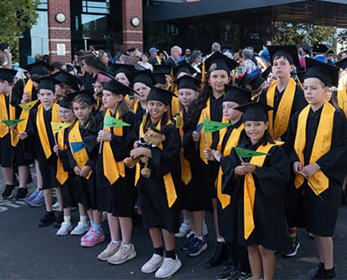 Children's University graduates in their caps and gowns, holding flags and walking in the South West Graduation 2025 Street Parade