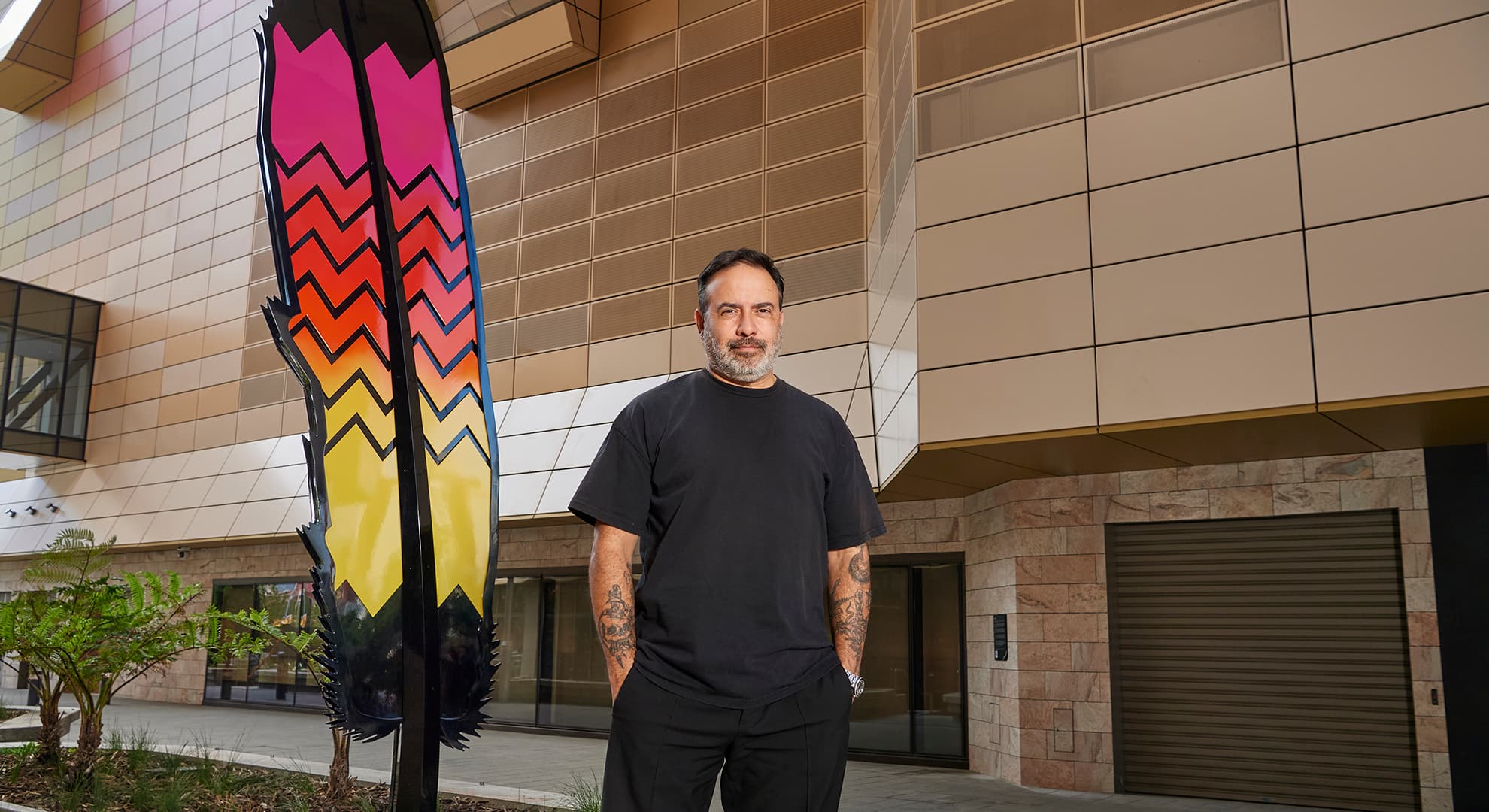 Man in black standing in front of a metal feather.