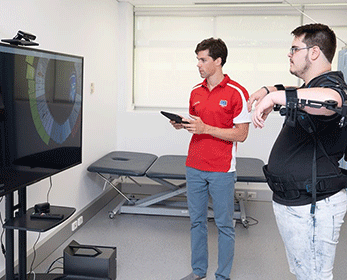 To target improvement in arm and cognitive functions, participants play a game with their arms supported by an exoskeleton.