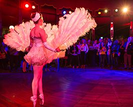 A dancer wearing feathers and sequins stands stage left looking out into an amphitheatre.