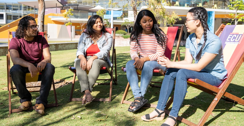 students sitting on chairs on the grass chatting.