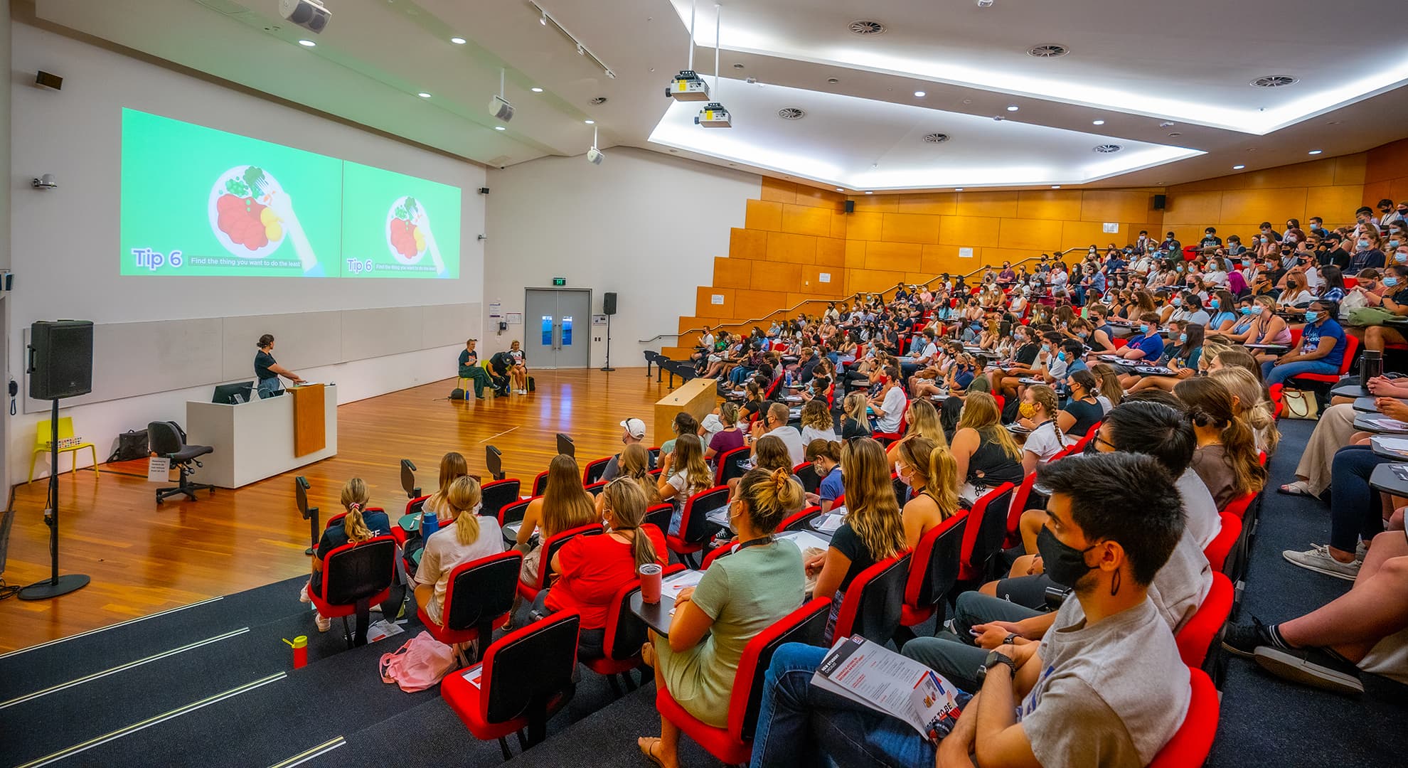 Lecture theatre full of students with people presenting information on stage