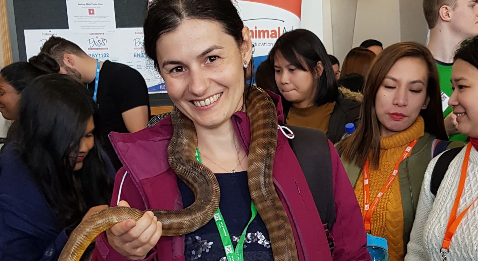 Andra Dinu holding a snake at ECU's international student Orientation in 2019. Maisha pictured just behind her right shoulder.