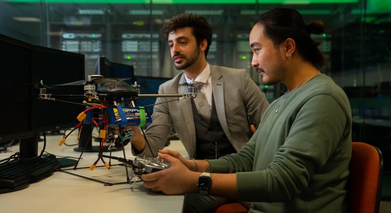 Two students examining a drone in a lab setting.