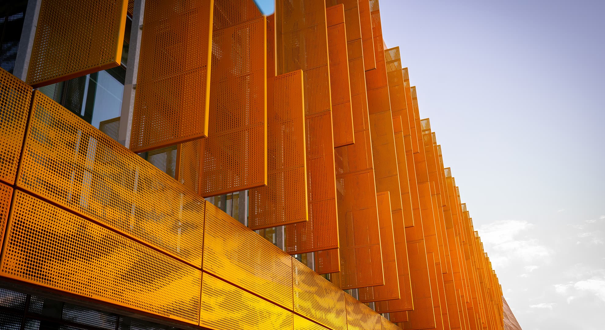 The exterior of a building with gold paneling in the sunlight.