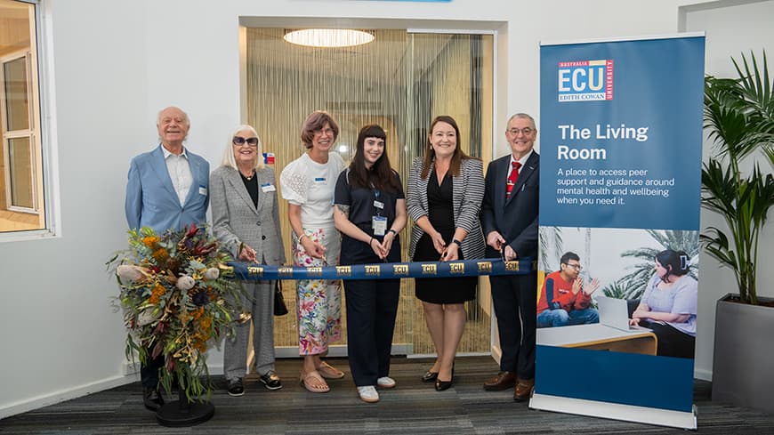 6 people lined up cutting an official ECU ribbon with 'The Living Room' banner on the right of the image