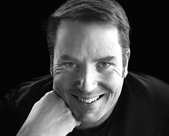 Professional portrait image in black and white of Professor Aaron Jarden smiling at the camera.