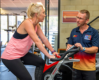 A gym instructor speaks to a lady on an exercise bike