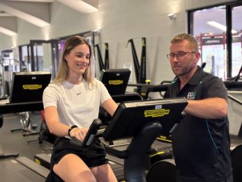 A gym instructor speaks to a lady on an exercise bike
