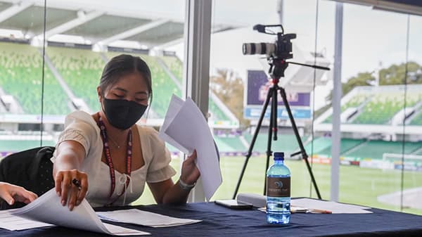 Katrina sitting at a table in an office a looking out over a sports oval.