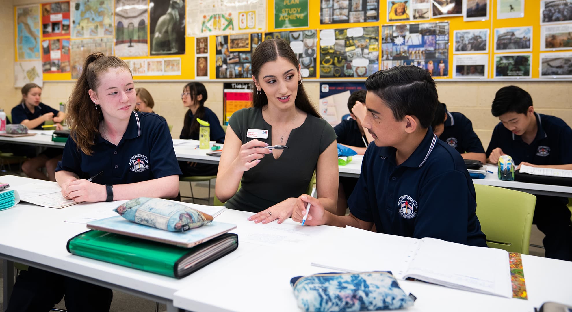 Young female teacher sitting in classroom with two students.