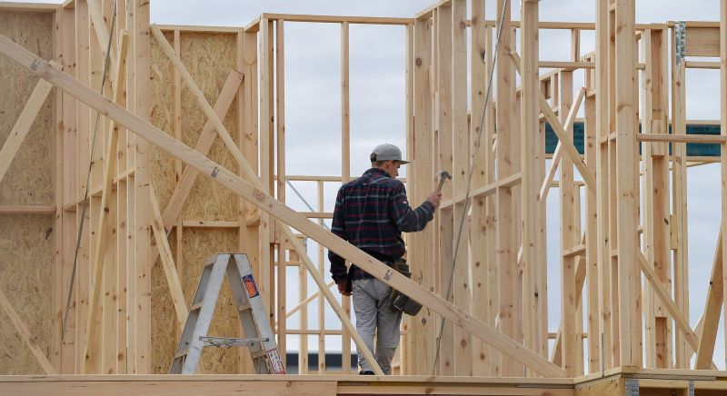 A builder walking through the timber frame of a house.